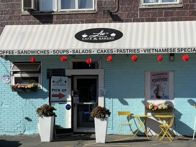 The original Lu's Cafe & Bakery storefront in Lawrence, MA — aqua brick facade with red lanterns and yellow bistro chairs