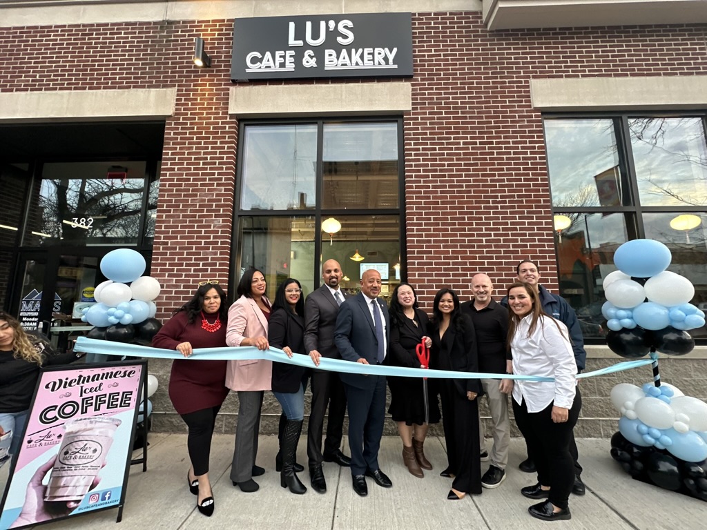 Lu's Cafe & Bakery ribbon cutting at 384 Essex St in Lawrence, MA — team and city officials with an aqua ribbon