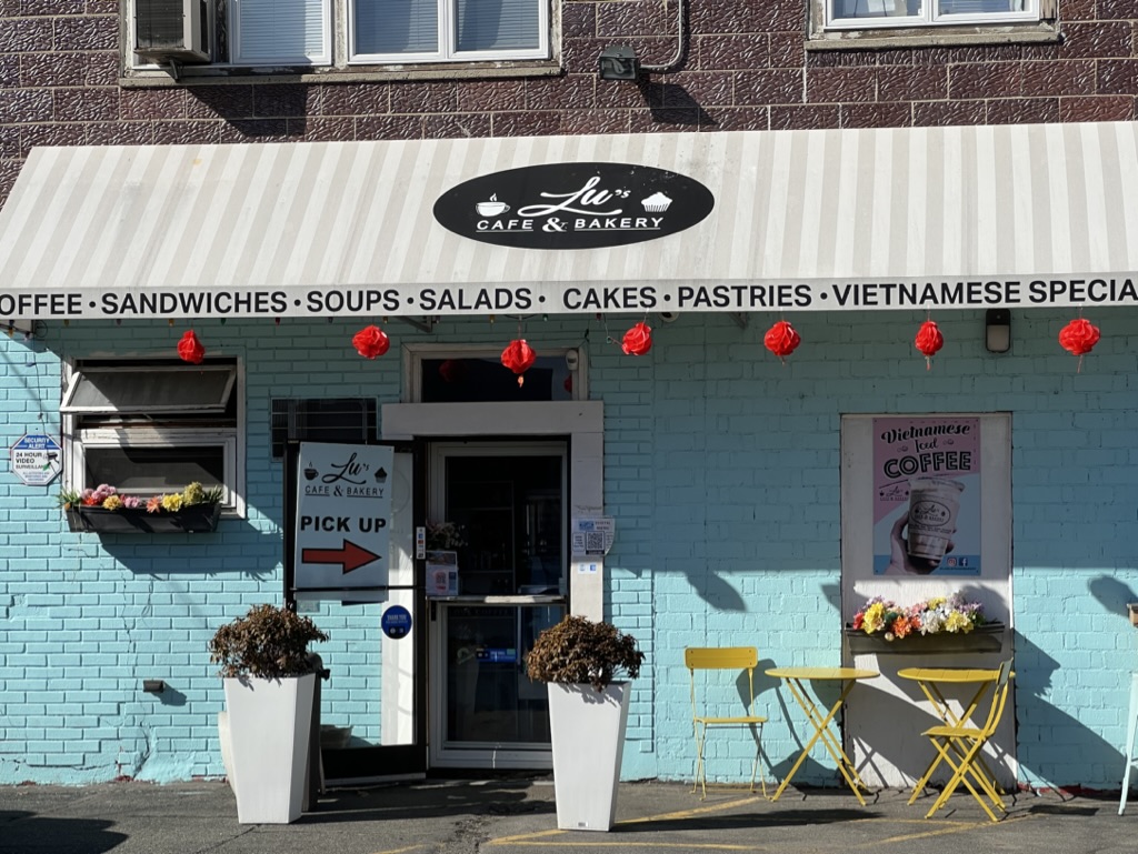 The original Lu's Cafe & Bakery storefront in Lawrence, MA — aqua brick facade with red lanterns and yellow bistro chairs