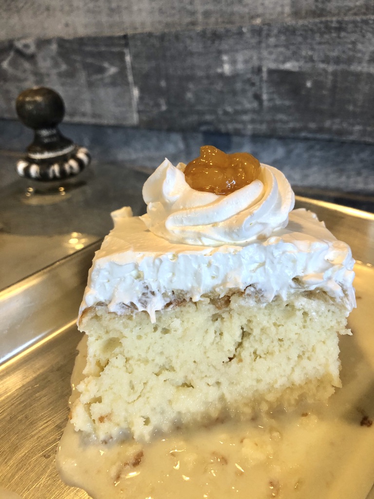 Slice of housemade tres leches cake with whipped cream and dulce topping at Lu's Cafe & Bakery in Lawrence, MA