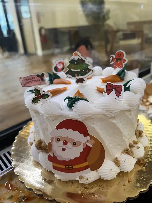 Christmas custom cake with a Santa design, holly, and holiday toppers by Lu's Cafe & Bakery